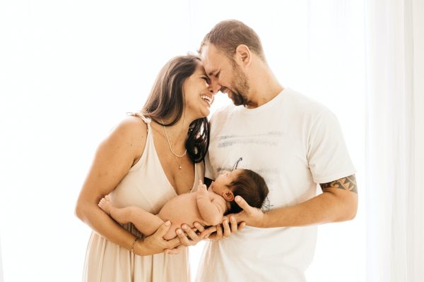 Smiling couple standing close, holding their newborn baby together.