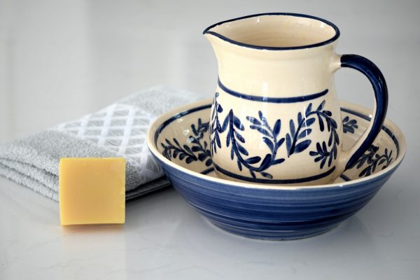 Ceramic pitcher and bowl with blue floral design, yellow soap, and folded towel on a white surface.