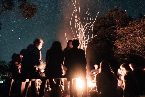group of people sitting around bonfire under night sky, their faces glowing