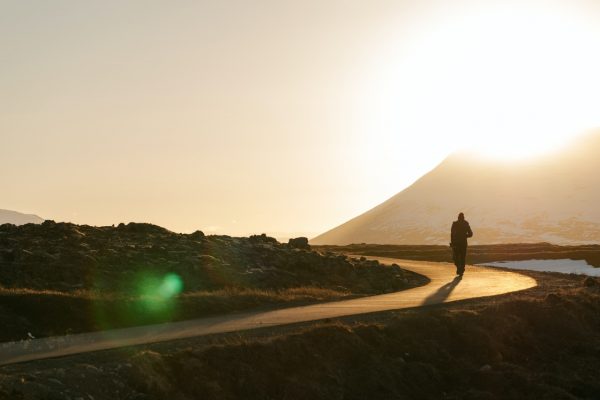 Person walking on a path toward the sunrise, with a mountain in the background.