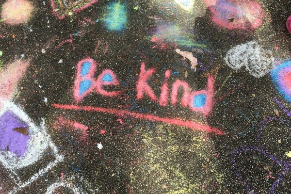 Colorful chalk drawing on pavement with the message Be Kind in pink and blue.