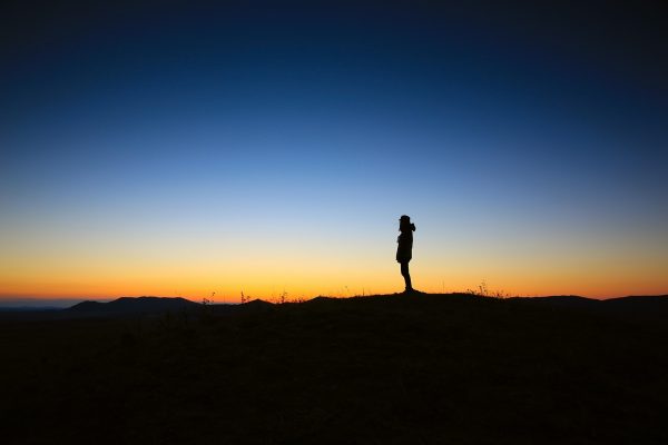 a person's silhouette in the distance underneath an indigo sky with a setting sun