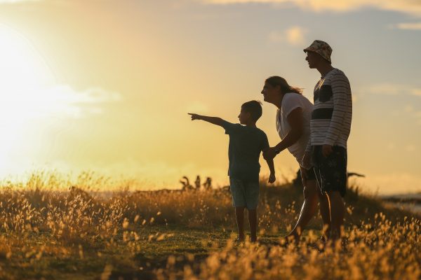 A family stands in a field at sunset, as a child points toward the horizon.
