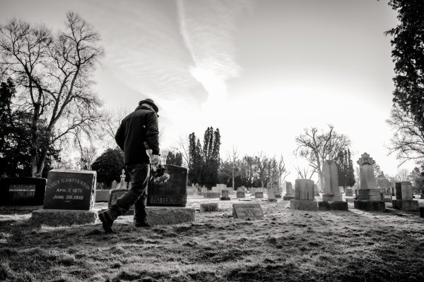 man bringing flowers to grave in cemetery