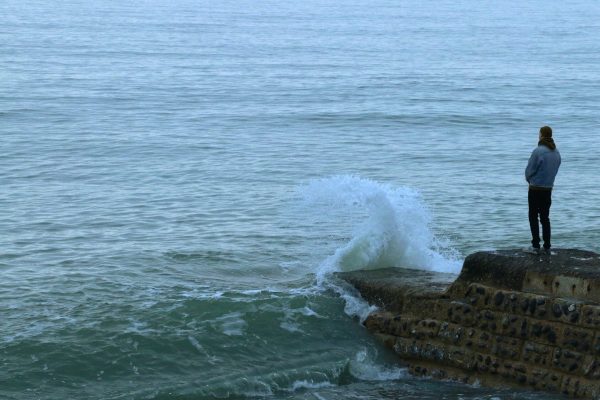 man standing on rocks looking at waves in water