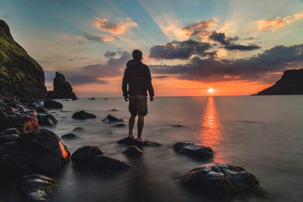 man standing on rocky beach at sunset