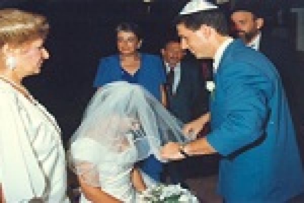 A groom lifts the veil of a bride surrounded by standing guests at a wedding ceremony.
