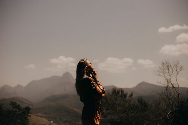 Silhouette of a person standing in nature, looking up at a cloudy sky with mountains in the background.