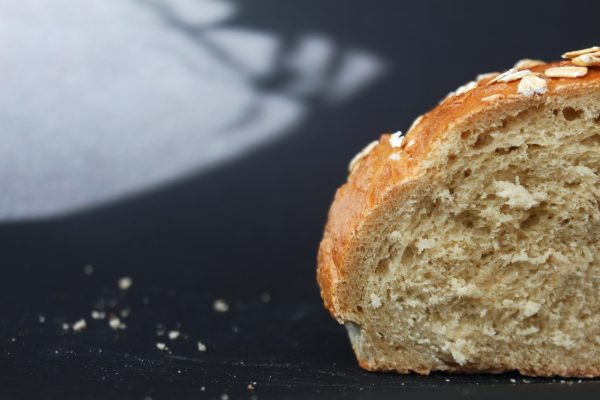 Close-up of a sliced bread loaf with oats on top, crumbs scattered on a dark surface.