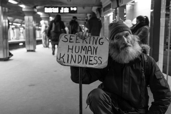 A man in a subway station holds a sign that reads Seeking Human Kindness.
