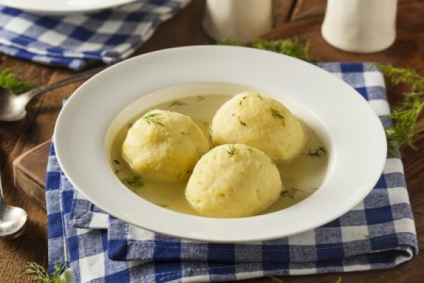 Three dumplings in broth on a white plate, set on a blue and white checkered napkin.