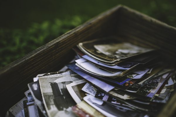 A pile of old, assorted black-and-white and color photographs is placed in a wooden box.