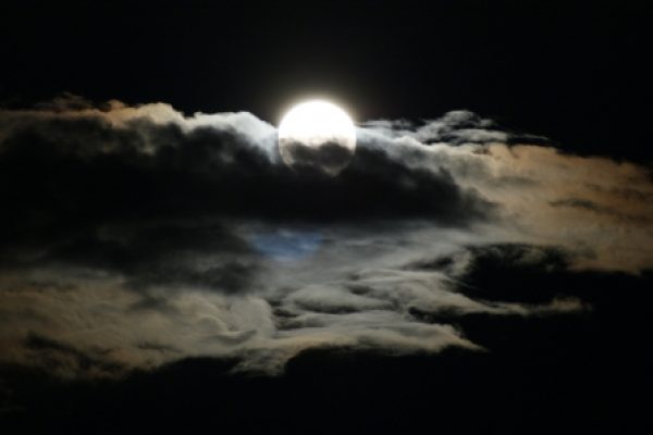 Full moon shining through dark clouds in a night sky.