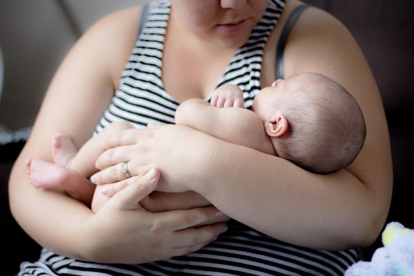 A woman in a striped tank top cradles a sleeping newborn baby in her arms.