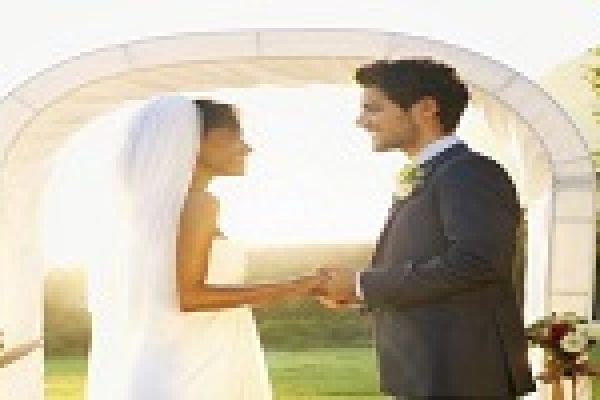 Bride and groom holding hands and smiling at each other under a wedding arch.