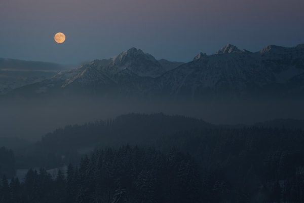 a full moon over mountains at twilight