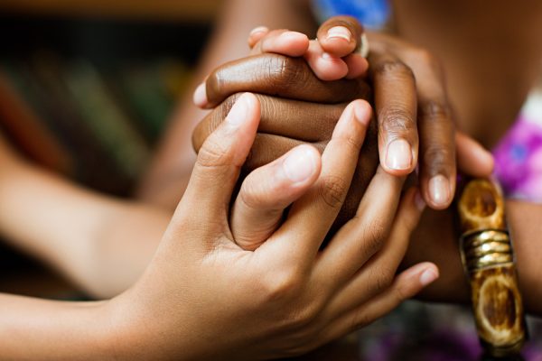 Close-up of diverse hands gently holding each other, symbolizing unity and support, with blurred background.