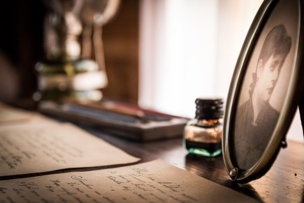 A framed portrait, ink bottle, and handwritten letters on a wooden desk.