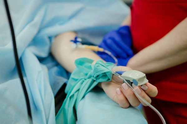 closeup of white arm with an IV in it in a hospital bed with person standing near bed
