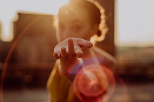 Person reaching towards the camera with blurred background and sun flare effect.