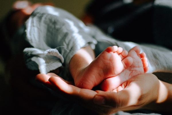 Close-up of a babys feet cradled in an adults hands, wrapped in a soft blue blanket with warm lighting.
