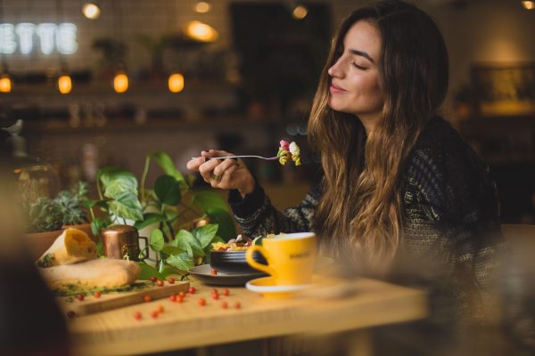 Woman enjoying a meal at a cozy cafe, with a yellow cup and green plants on the wooden table.
