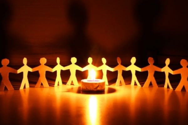 Paper cut-out figures holding hands around a glowing candle in a dark room.