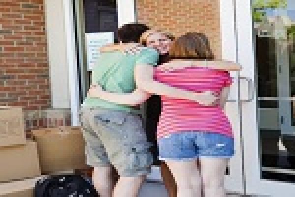A group of people hugging outside a building, with cardboard boxes nearby.