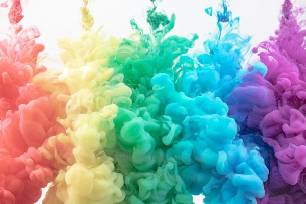 Vibrant clouds of colorful ink swirling in water, creating a rainbow effect against a white background.