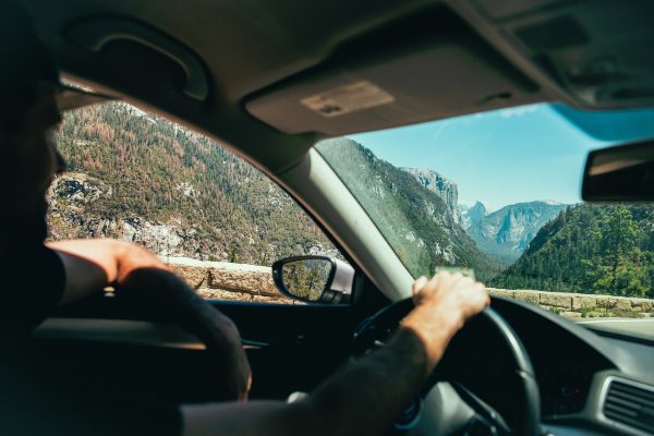 Person drives a car through a scenic mountain area with trees and cliffs visible through the windshield.