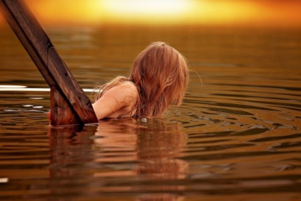 Child climbing out of a lake at sunset, with ripples in the golden water.