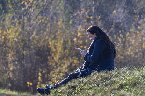 a woman sits on the grass looking at her phone