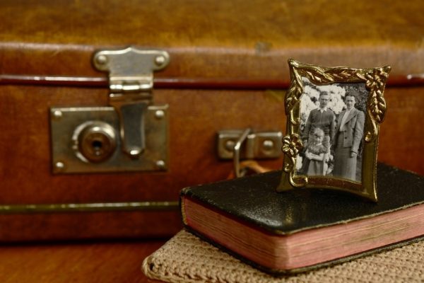 Vintage family photo in a gold frame on a book, with an old suitcase in the background.