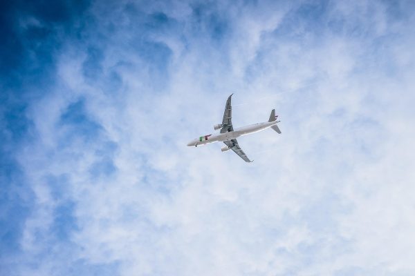 A commercial airplane flying through a cloudy blue sky, viewed from below.