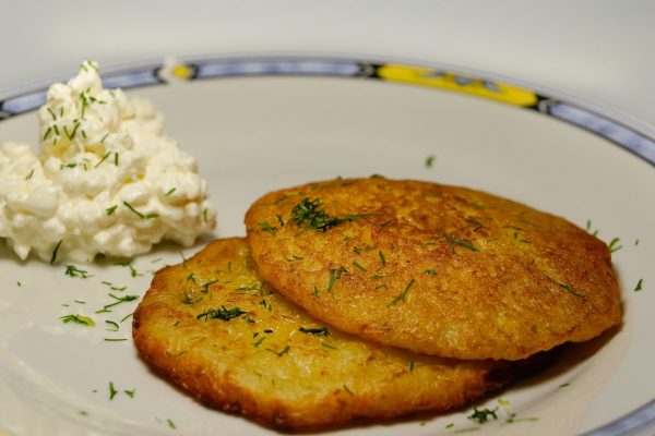 Two potato pancakes garnished with dill on a plate, served with a side of cottage cheese.