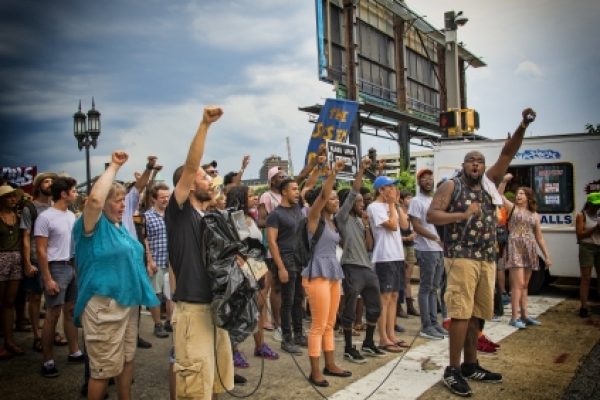 A diverse group of people protest on a street, raising fists and holding signs.