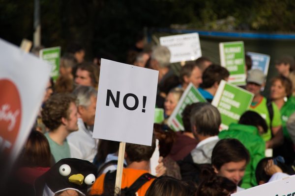 Crowd of protestors holding various signs, including one prominently displaying the word NO!.