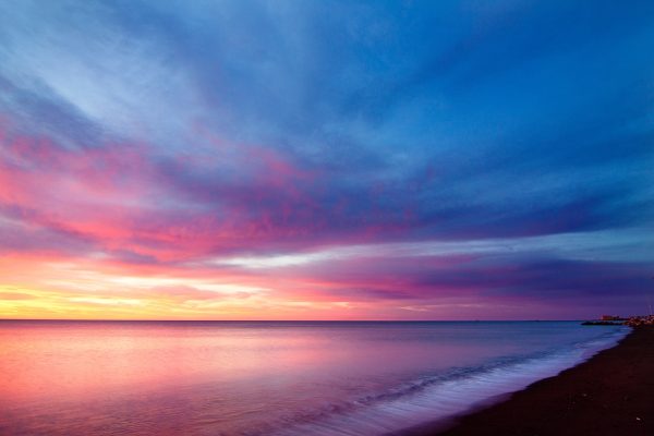Vibrant sunset over a calm ocean with a sandy beach in the foreground and colorful clouds in the sky.