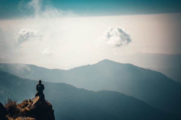 view of mountains in blue and white sky with clouds with person on a rocky outcrop small in the scene