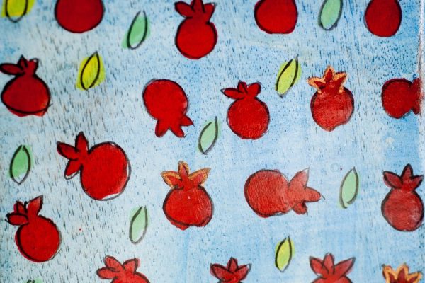 Red pomegranates and green leaves are scattered across a blue background in a playful, hand-drawn style.