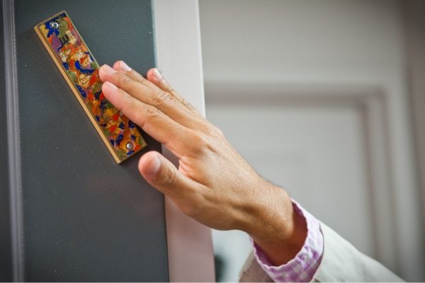 A hand touches a colorful mezuzah on a doorpost in a home.
