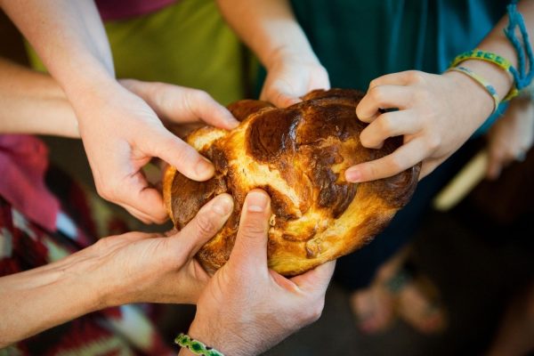 Several hands tearing a round loaf of bread, symbolizing sharing and togetherness.