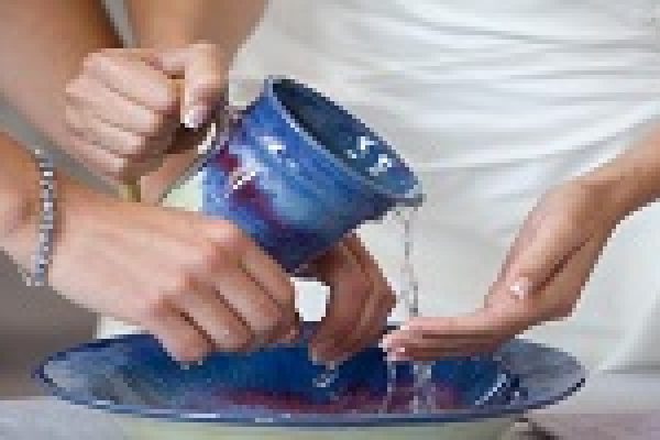 Close-up of hands pouring water from a blue ceramic jug into a matching bowl, symbolizing a ceremonial act.