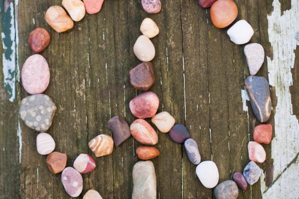 Peace sign made of colorful stones arranged on weathered wooden surface with peeling white paint.