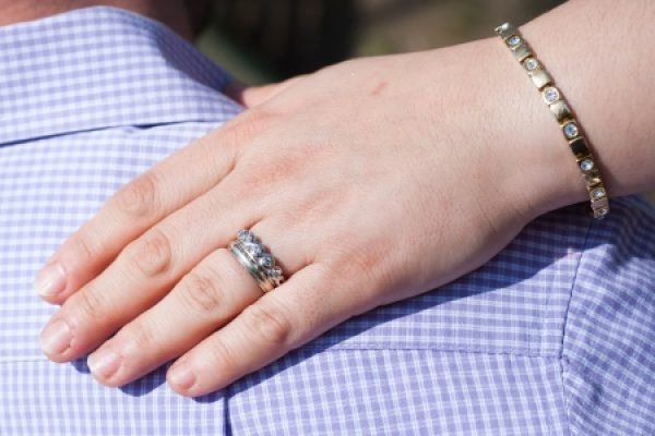A hand with a ring and bracelet rests on a persons shoulder wearing a purple checkered shirt.