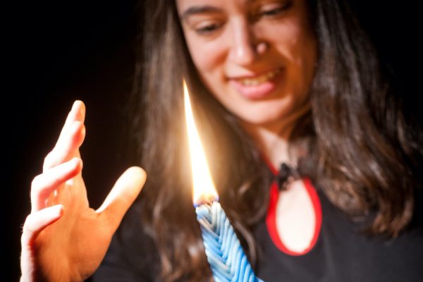 Person smiling near a lit candle, reaching out a hand towards the flame.