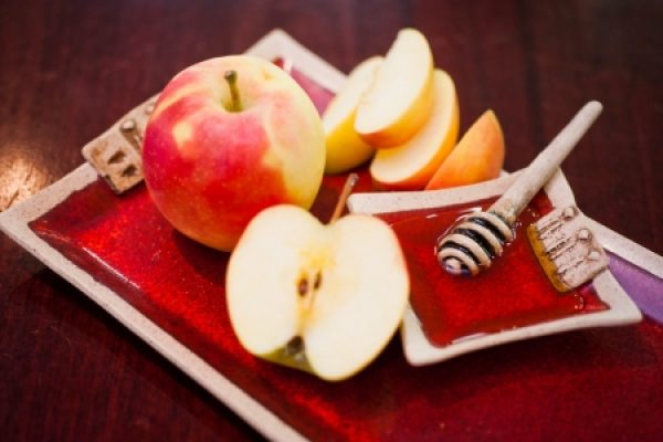Apple whole and sliced on a red tray with a honey dipper.