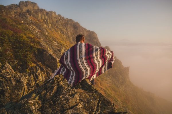 young man wrapped in colorful blanket climbing mountain in the desert