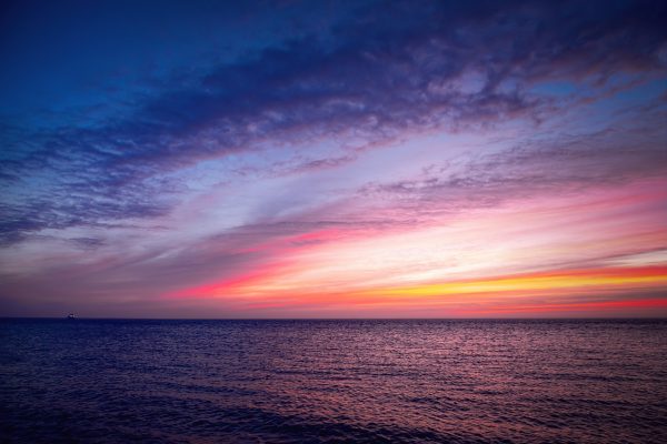 Vibrant sunset over a calm ocean, with pink, orange, and purple hues blending into a darkening sky.