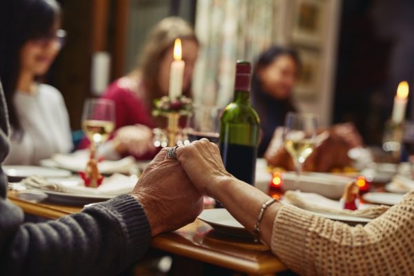 People holding hands at a dinner table, with food, wine, and a lit candle.